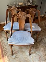 Six wooden dining chairs with carved backs and attached light blue cushions arranged in a room.