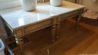 Overall view of one of the end tables showing marble look top and gilded base with tapered legs.