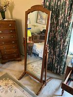 Full frontal view of the full length wood framed mirror standing on carpet near floral curtains and wooden dresser.
