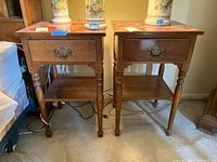 Front view of two matching Ethan Allen side tables with drawer and lower shelf, showing wood finish and brass handles.
