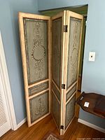 Three-panel folding screen shown partially folded in a standing position, showing the overall structure and size.