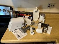 Overview of all items on kitchen counter including Krups grinder, Chef's Choice sharpener in box, an electric coffee pot, an electric can opener, and a coffee grinder with attachments and manual visible.
