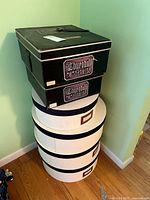 Six hat boxes stacked; four white round boxes with dark rims and two black rectangular Churchill Hats Ltd boxes stacked at top.