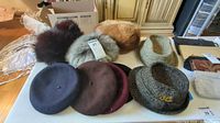 Overview of all hats folded or grouped on the table showing diverse styles including fur look, wool berets and tweed hats
