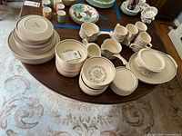 Wide view of the entire Lenox Temper-ware Blue Breeze dinnerware and serving set spread out on a table, showing stacks of plates, bowls, cups, and pitchers.