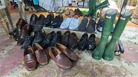 Overview of all men's brown and black leather dress shoes and loafers, plus white casual shoes and green welly boots on carpeted floor beneath rack.