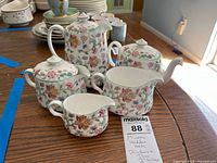 Minton Haddon Hall tea set displayed on wooden table showing the entire set of pots and pitchers with floral décor.