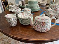 Wide image showing the entire tea service spread out on the table, including stacked plates, cups, saucers, and teapot with lid.