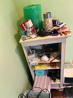 Small white shelving unit with various office supplies including tape rolls, paper clips, fly swatters, bubble wrap and packing paper.