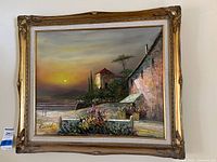 Full view of the framed oil painting depicting a sunset coastal scene with architectural elements and vegetation