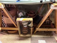 Wooden shelves with various terracotta and ceramic planters stacked; a vertical rectangular wooden-framed metal sieve in front of pots.