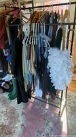Photo showing various scarves on hangers on a garment rack including dark wool/cashmere scarves, a white feather boa, and a black formal robe.