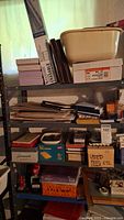 Wide view of metal shelf with various stacks of notepads, boxes for used pens, envelopes, and other stationery supplies