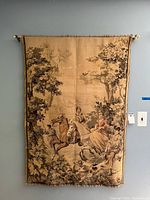 Full view of vintage hanging tapestry on wall, showing pastoral scene with figures on horseback and trees