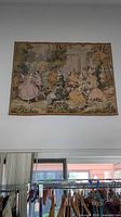 Full wall view of large tapestry hanging indoors above clothing racks