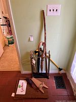 Metal umbrella stand with umbrellas, walking stick and boot jack against a wall on tile floor