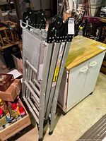 Photo showing folded WestWay professional adjustable aluminum ladder standing next to white cabinet and other basement items.