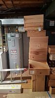 Stack of 20 wooden wine boxes in a basement near a water heater, showing box dimensions and unfinished wood texture.