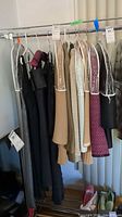 Various women's two-piece suits and dresses hanging on rack, protected by garment covers.