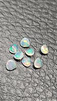Nine small faceted pear cut natural Ethiopian opals on black textured background showing multicolored flashes.