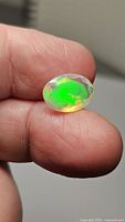 Close-up photo of oval cut faceted Ethiopian opal held between fingertips showing vibrant green and blue color flashes.