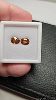 Close-up photo of two oval-cut Cambodian Zircon gemstones in a white display box with visible bright deep champagne orange color.