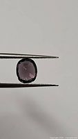 Photo showing the natural spinel gemstone held in tweezers, displaying its cushion cut shape and deep purple color with good transparency and color play.