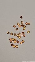 Top-down clear photo of multiple small round cut imperial orange sapphires arranged scattered on a plain surface, showing color and size of the stones.