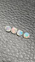 Four cushion cut natural Ethiopian opals with vibrant rainbow fire on black textured background.