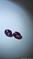 Two oval cut sapphires showing a deep raspberry purple-pink color under light.