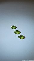 Three pear cut natural apple green peridot gemstones arranged on a white background, showing color and cut.