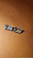 Pair of emerald cut aquamarine gemstones viewed at an angle on a textured brown surface showing color and cut