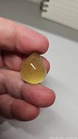 Hand holding a large natural lemon yellow citrine pear cabochon gemstone showing smooth polished surface and bright color.