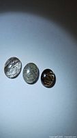 Three oval cabochon cut natural black rutilated quartz gemstones placed on a white surface under focused lighting.