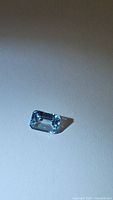Close-up photo of 1.09 carat sky blue topaz emerald cut gemstone on a white background with shadow visible.