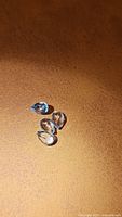 Four natural sky blue topaz pear cut gemstones displayed on a brown surface.