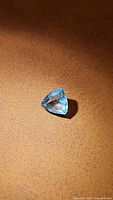 Close-up image of a blue trillion cut aquamarine gemstone on a brown textured surface, showing facets and color