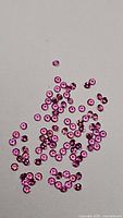 Photo showing scattered small round calibrated cherry blossom pink sapphires on a gray surface.