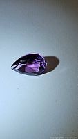 Photo of a deep purple pear cut amethyst gemstone with visible facets and good clarity photographed on a plain surface.