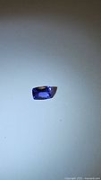 Photo showing deep blue cushion cut Tanzanite gemstone on a light surface with natural shadows to highlight facets and clarity.