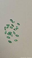 Photo showing multiple small marquis cut natural emerald gemstones spread on a white background.