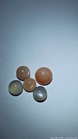 Five natural moonstone cabochons of mixed colors on plain background.