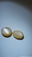 Two oval natural peach moonstone cabochons shown under angled lighting to highlight their flash and semi-translucent peach coloration.