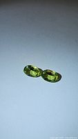 Matching pair of oval cut natural apple green peridot gemstones displayed side-by-side on a white background.
