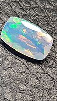 Close-up image of cushion cut Ethiopian opal showing vibrant rainbow colors and facets on textured black background.