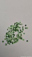 Multiple small natural tsavorite garnet gemstones scattered on white background, vivid green color visible.