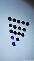 Top-down photo showing 15 round-cut royal blue sapphires scattered on a white surface, displaying their deep color and clarity.