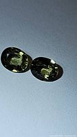 Pair of oval cut green sapphires with yellow undertones shown in close-up on a plain background.