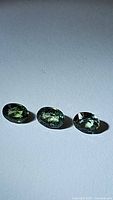 Three oval-cut natural sapphires with green body and subtle yellow and blue undertones, showing multicolored effect under light.