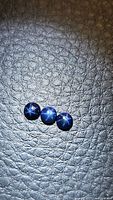 Three round natural blue star sapphire cabochons placed on textured black background showing their star effect under light.